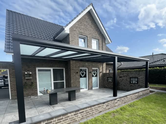 Premium-Terrassenüberdachung aus Aluminium mit großer Spannweite und Glasdach an einem Klinkerhaus – Terravista Meppen